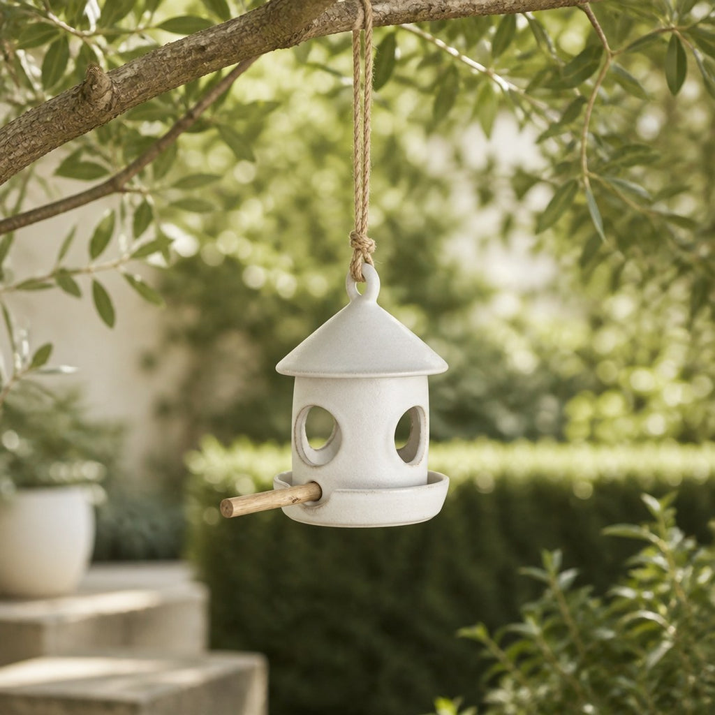 Ceramic bird feeder hanging from a tree branch in a garden