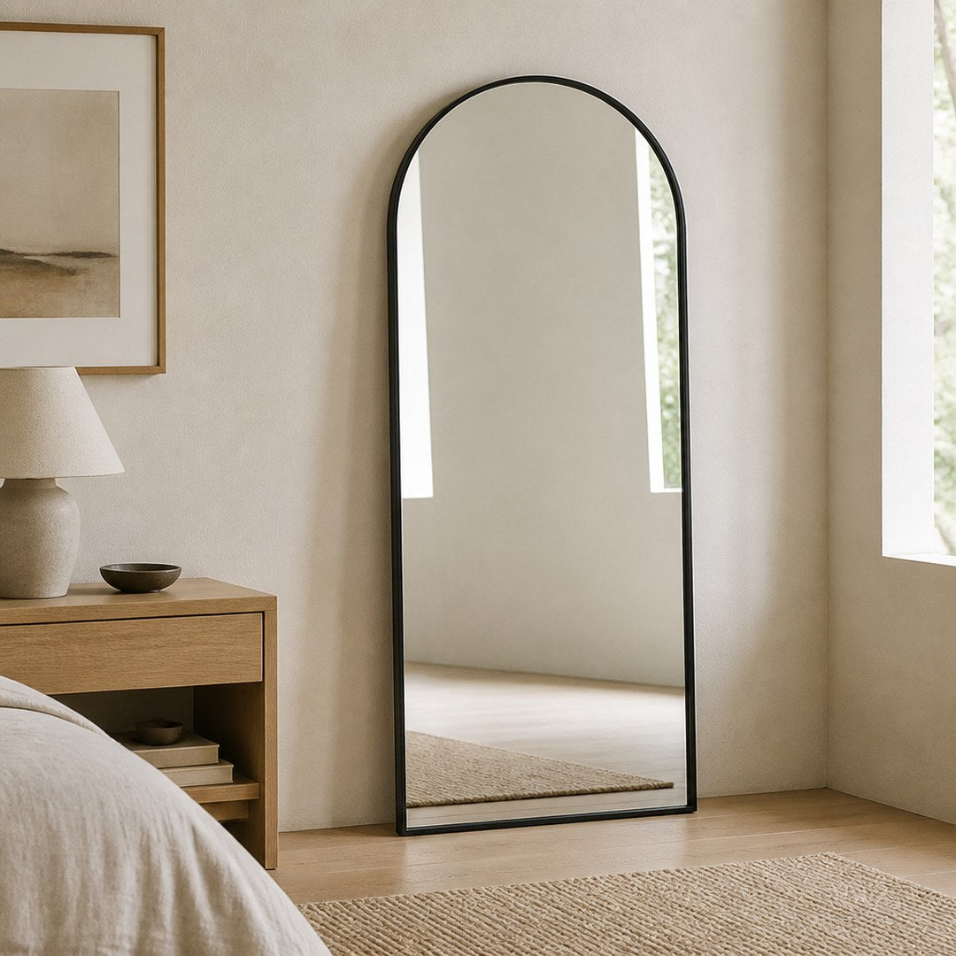 Arched wall mirror leaning against a bedroom wall beside an oak nightstand